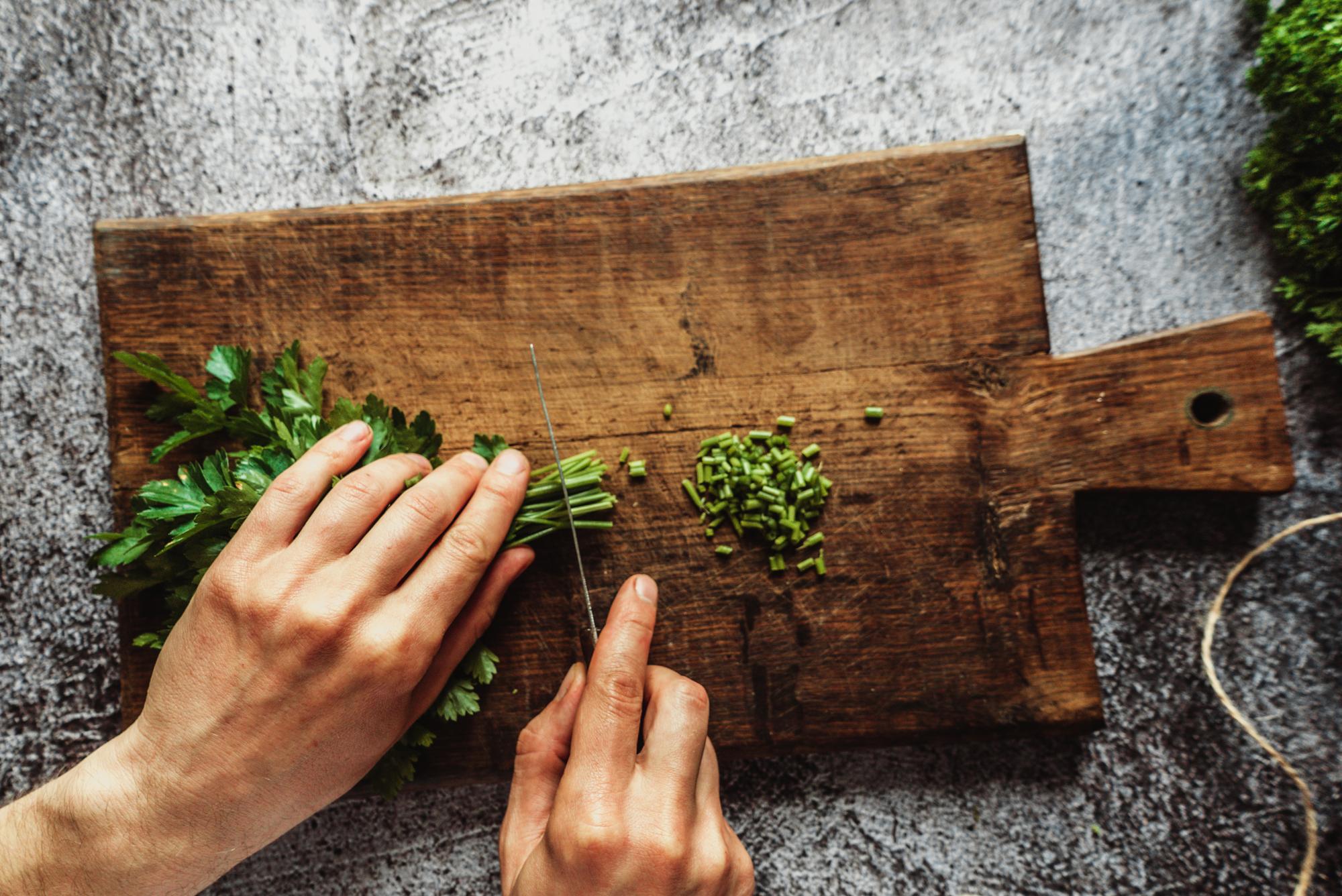 hands chopping fresh herbs on wooden board